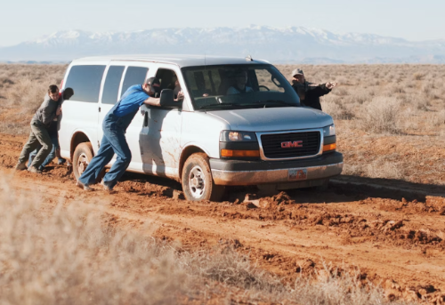 Men help roadside assistance staff push a car stuck in the mud