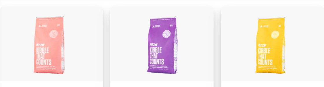 Three bags of Petzyo dry dog food that are pink, purple and yellow on a white background