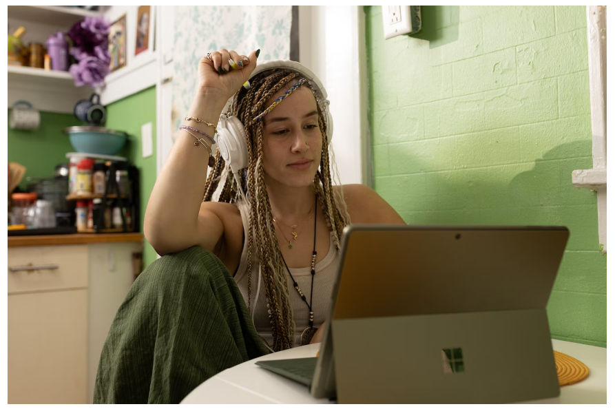 A female college student with headphones browsing on her laptop for a Grammarly promo code to use