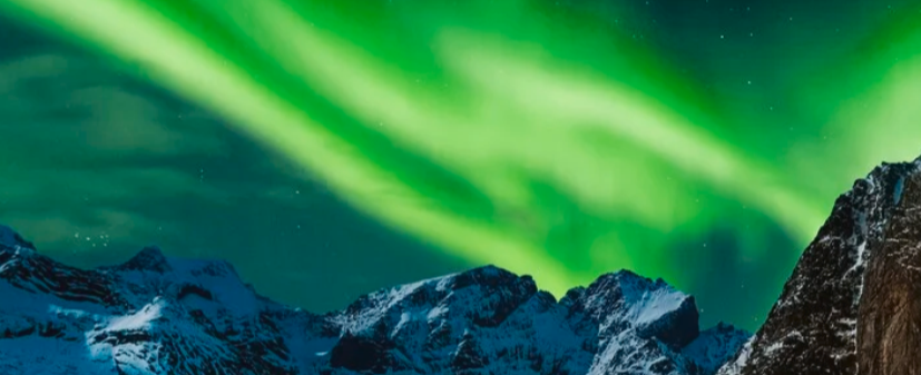 Grünliche Nordlichter mit ein paar schneebedeckten Bergen darunter