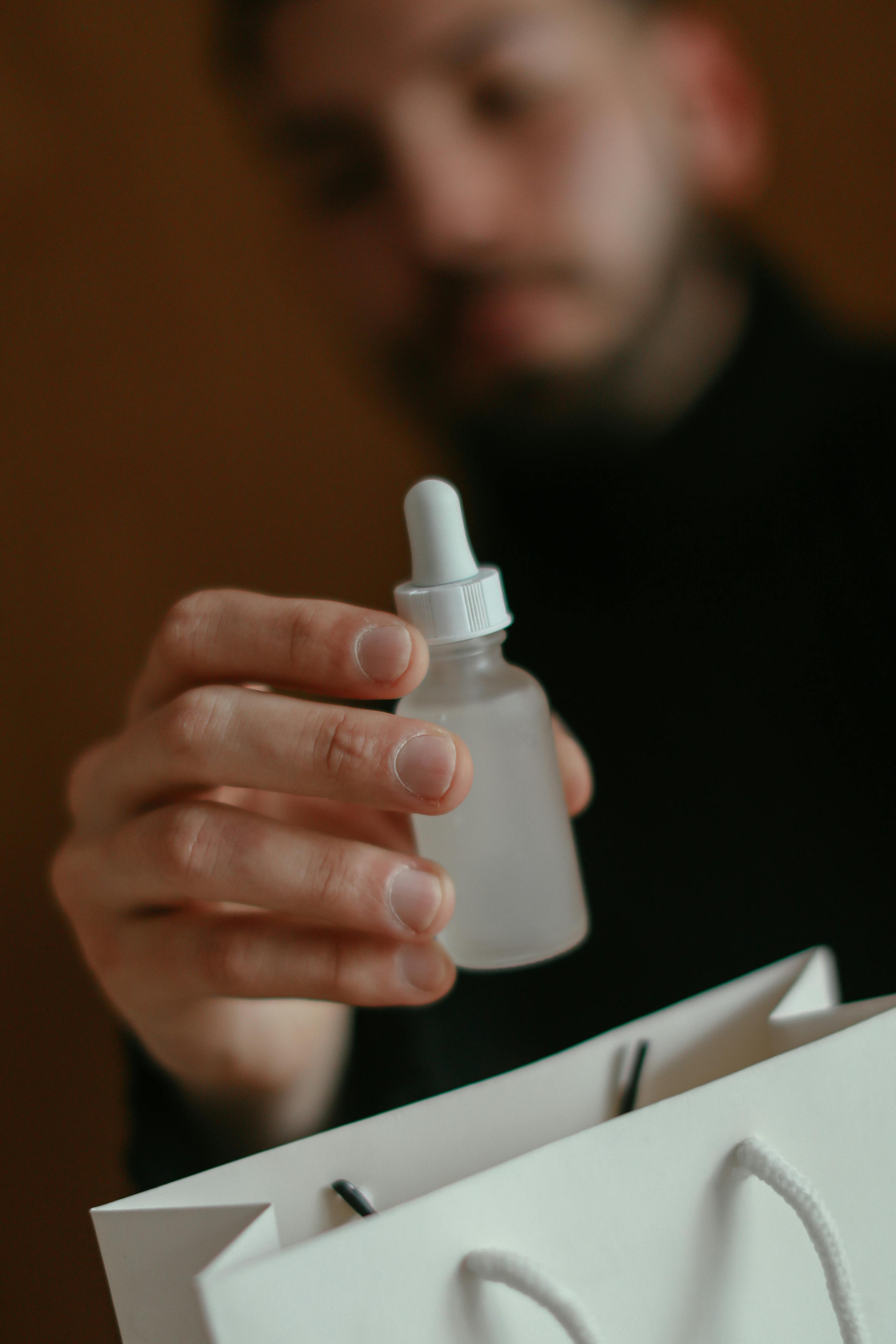 A man holding an oil bottle in his hand with a white gift bag on the side.