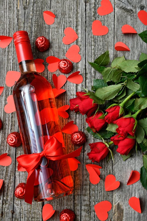 A bottle of wine surrounded by chocolates, paper hearts and roses