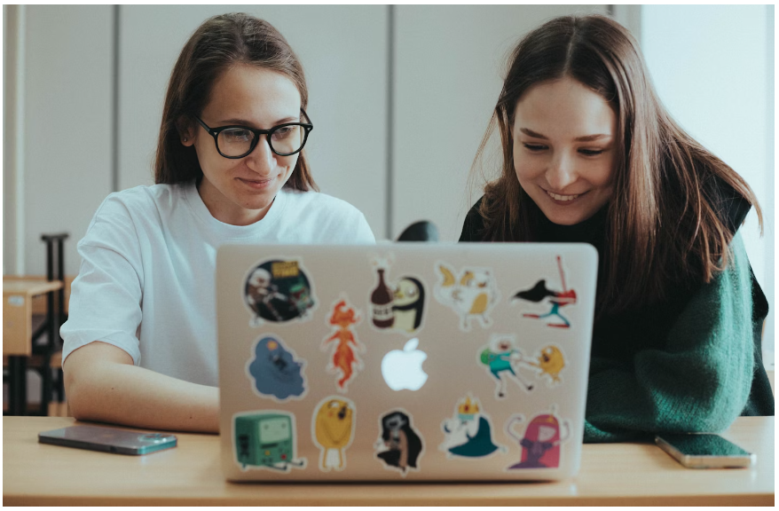 Two female students scrolling on their laptop for a White Fox discount code to shop