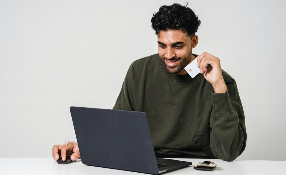 Man holding a card. He is busy on a laptop. He is smiling due to finding a eBay promo code.