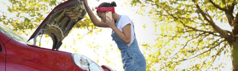 lady looking inside the bonnet of a red car looking drstressed on the phone
