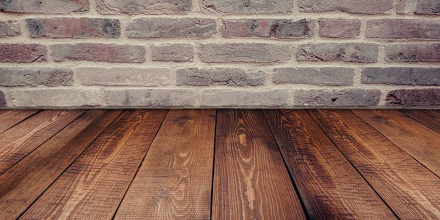 Dark oak wood panel flooring laying next to a dark brick wall