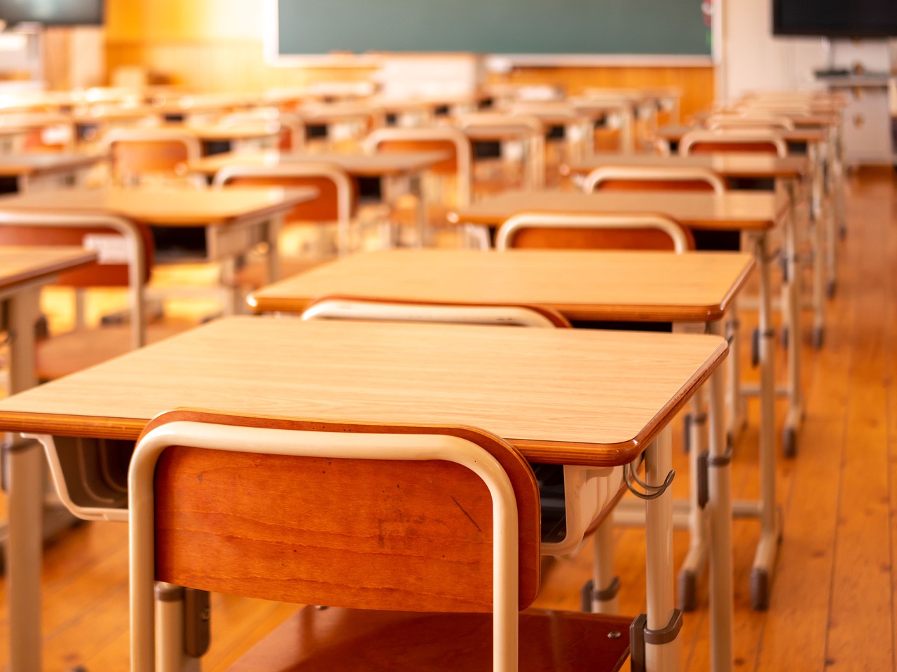 mesas y sillas de colegio de color madera en un aula de un colegio con mucha luz cálida