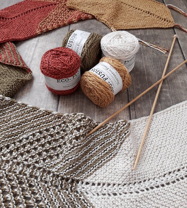 A pile of red, green, tan and white yarn rolled into tight balls next to a knitted scarf on the floor