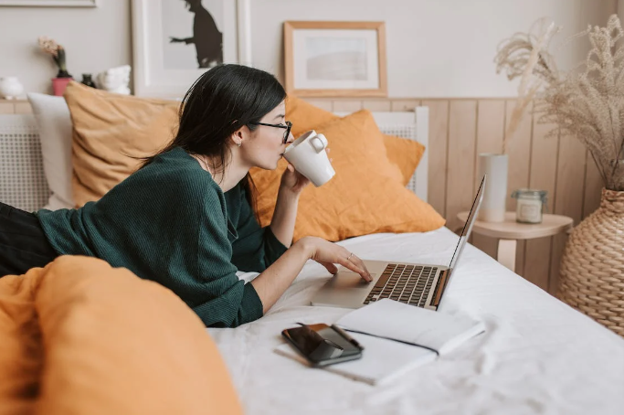 A girl on her bed searching for a Kiierr discount code on her laptop while drinking coffee.