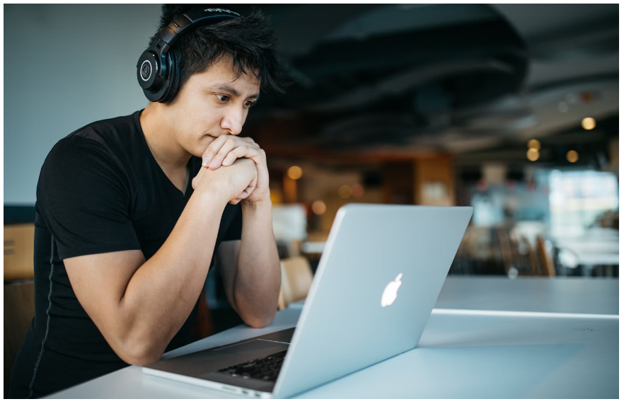 A male student looking at his laptop with headphones on his head for THE OUTNET promo code