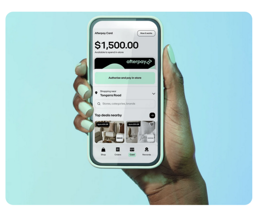 a hand on a blue background with white nail polish holding a mobile phone with an afterpay page displayed on screen