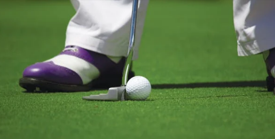A person in white pants playing golf wearing blue and white shoes on a golf course villa