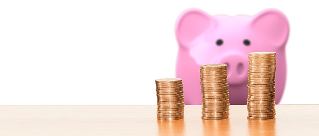 Three stacks of coins on a table in front of a pink piggy bank