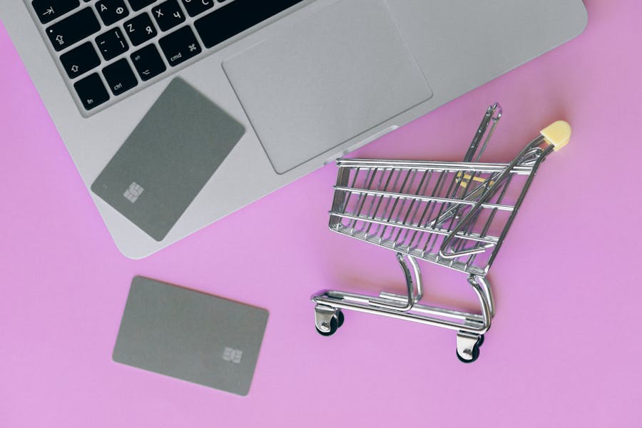 A silver laptop with 2 silver bank cards and a shopping cart all near each other