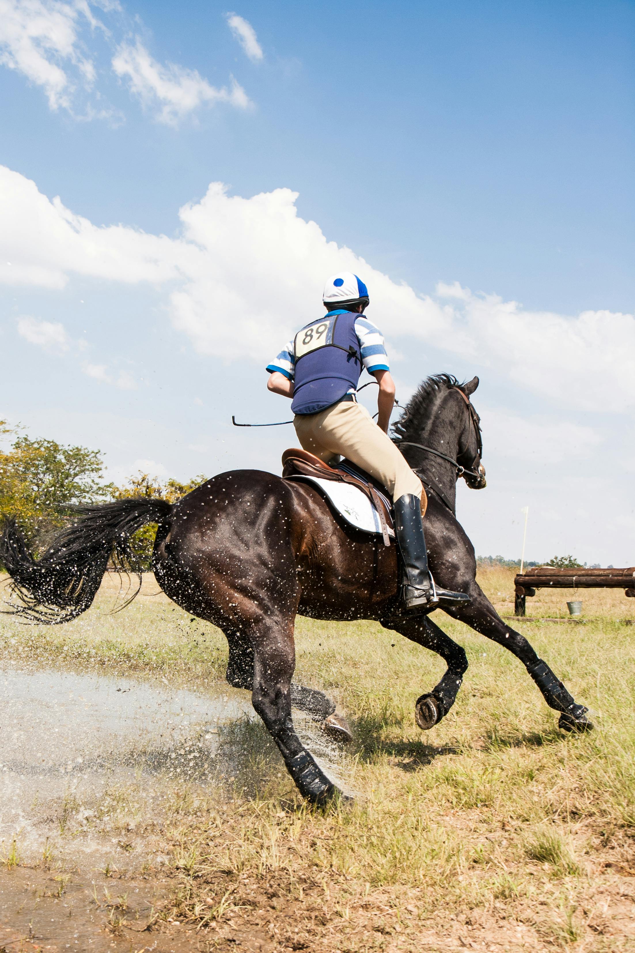 A young man riding a horse out in an open field wearing equestrian clothing.
