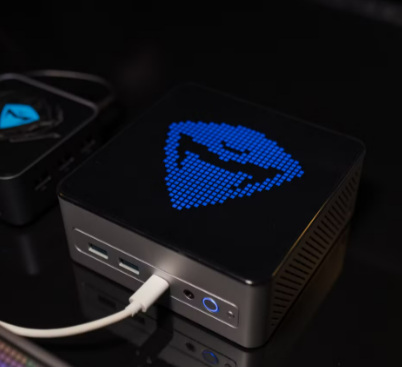 Compact GEEKOM mini PC with customizable digital display glowing in blue on a dark desk setup.