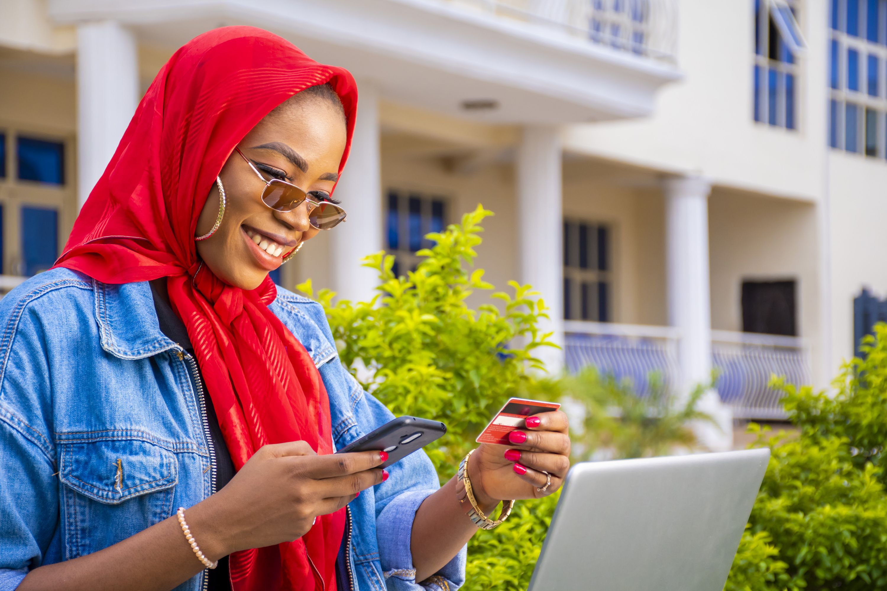 african-female-happily-shopping-online-using-laptop-smartphone-while-holding-her-credit-card
