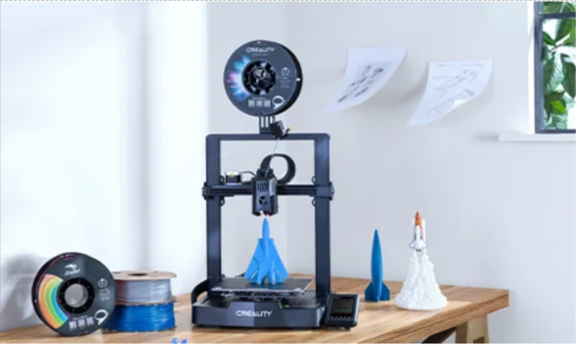 Ein offener 3D-Drucker auf einem Holztisch mit Filamenten und ein paar Figuren