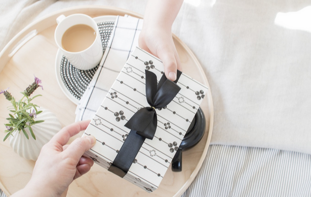 Eine Hand, die einer anderen Hand ein Geschenk in schwarzweißer Verpackung überreicht