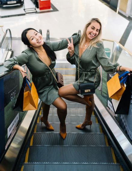 Two young ladies posing for a picture on an escalator and carrying Singles Day shopping bags