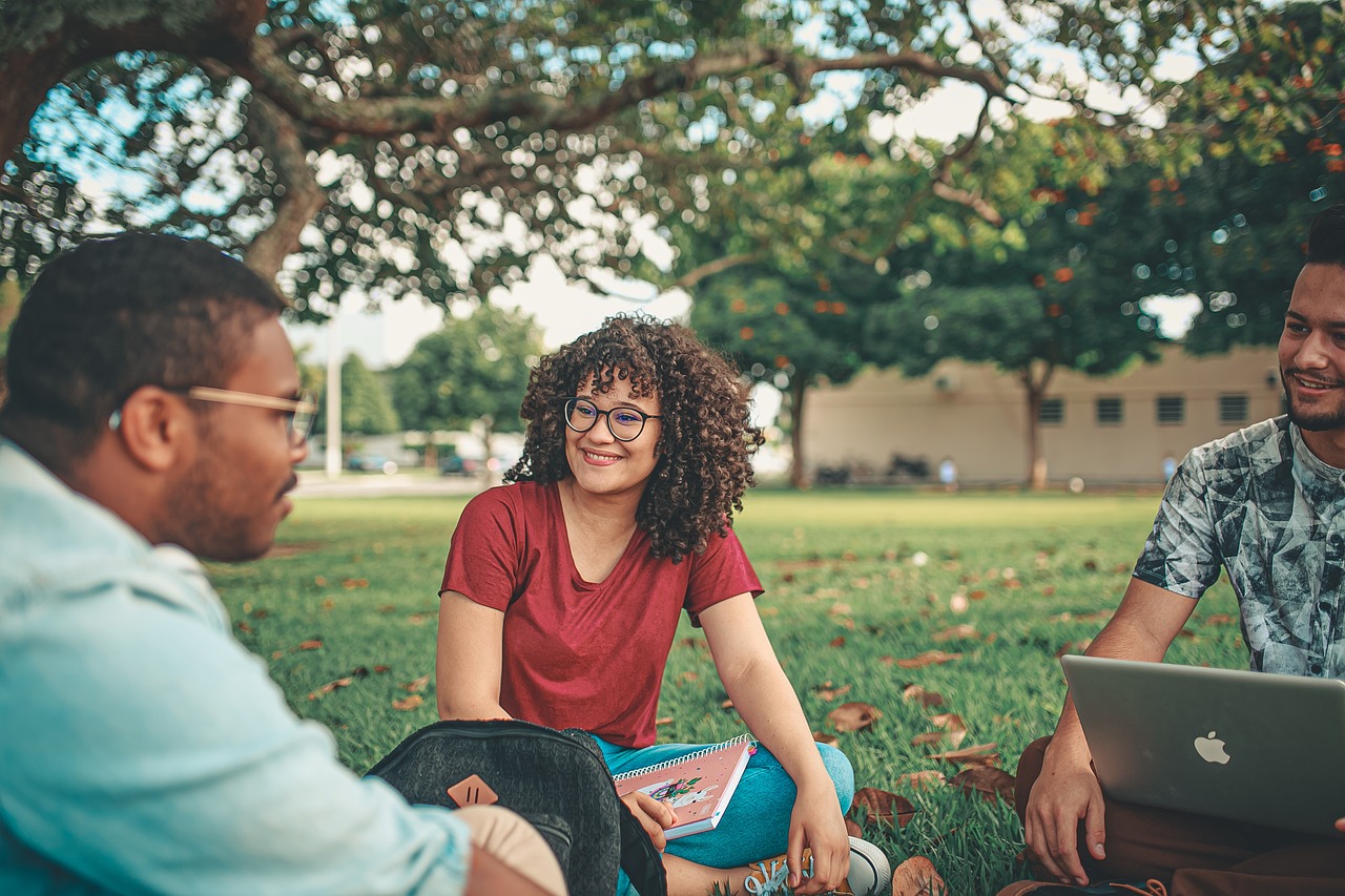 three students searching for Adultshop.com discount codes while sitting on a lawn on a university campus