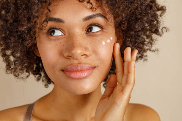 une jeune femme au cheveux bouclés avec trois goutes de crème sur le visage. elle est souriante, aimable et fraiche tout en pensant au code promo