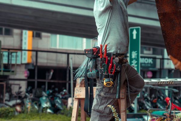 A handyman on a ladder wearing a tool belt with hand tools and a power drill