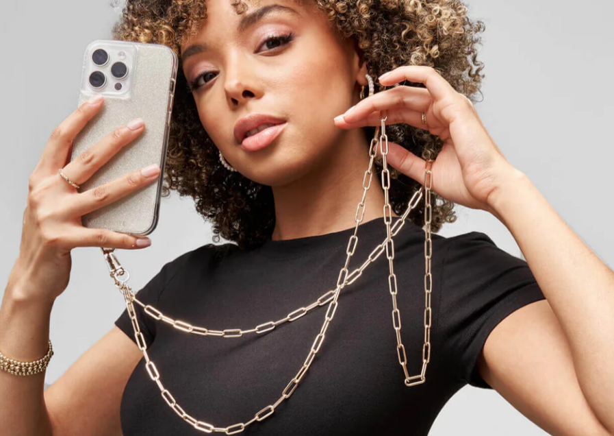 A woman wearing a black top posing with her glittery iPhone case and the crossbody chain