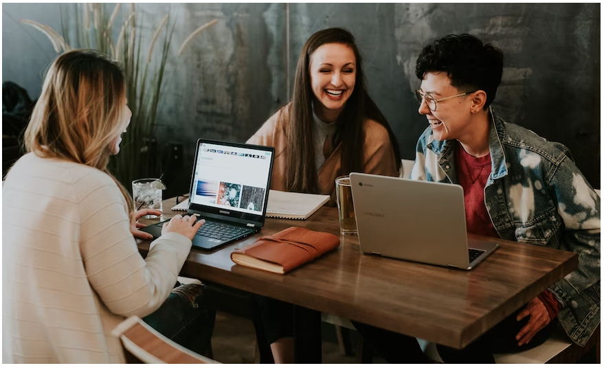 Two female and one male student with laptops and a notebook laughing over discounts at Mothercare