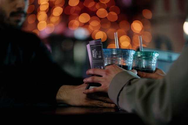 A bearded man handing out concert tickets and two soda-carbonated drinks to a customer
