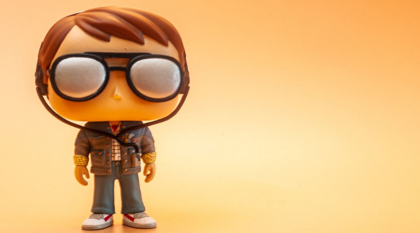 Eine stehende Funko Pop Figur mit großer Brille vor einem gelblichen Hintergrund