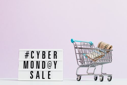 A white sign with "Cyber Monday Sale" on it next to a shopping cart filled with money