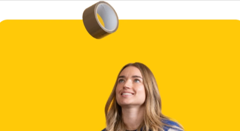 A woman with long blonde hair looking up at a cellotape up mid-air above her head