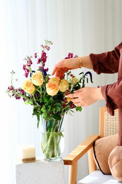 A person's hand arranging a bouquet of peach rose and purple flowers
