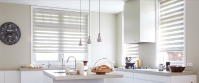 A modern kitchen with blinds on the windows, a wall clock, and kitchen accessories on the counter