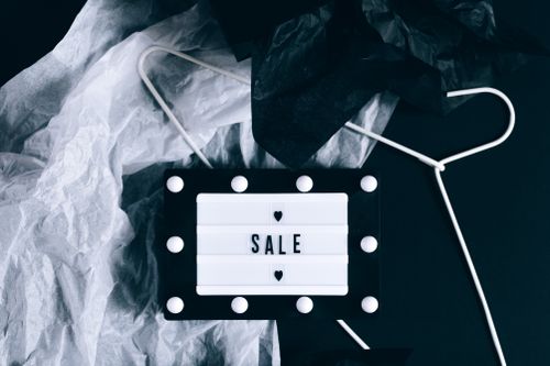 A black and white sign with the word "Sale" on it surrounded by packaging and clothes hangers