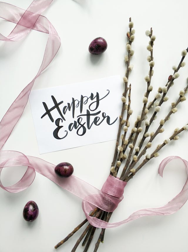 A note with Happy Easter on a table surrounded by flowers and chocolate eggs