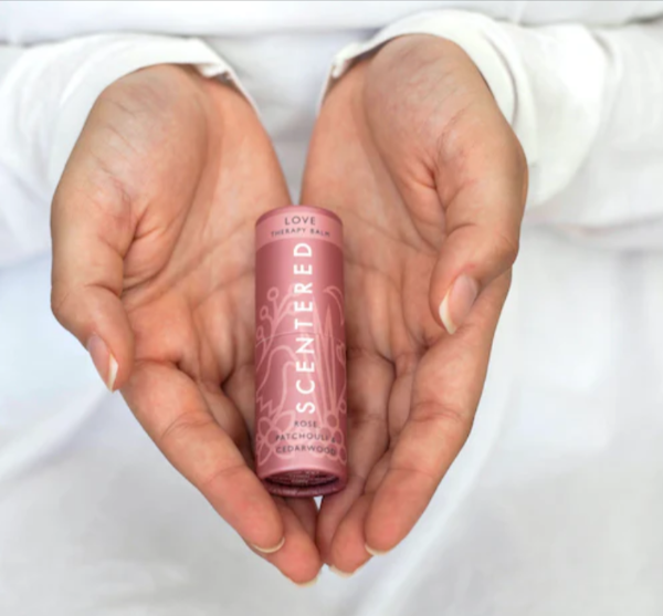 A lady dressed in white, with a Scentered aromatherapy balm in her hands