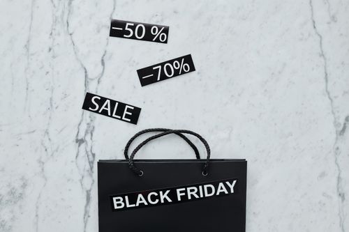 A black bag on a marble floor with "Black Friday" on it and banners with "-50%, -70% and Sale" coming out of the bag