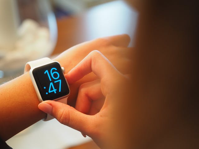 A person looking at their digital watch shwoing that the time is 16:47 pm.