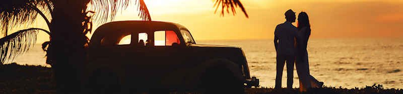 Ein Liebespaar vor einem Sonnenuntergang neben einem Auto und einer Palme