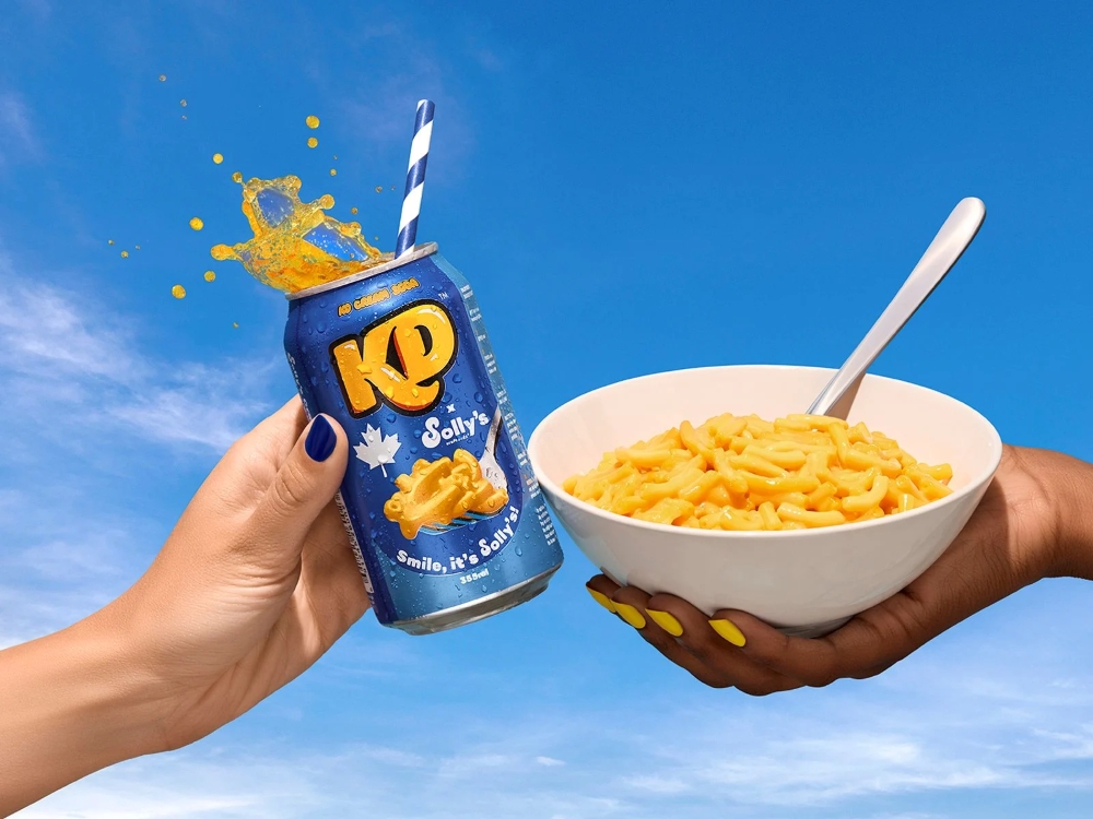 A KD x Solly’s Cream Soda and a bowl of Kraft mac and cheese held by two hands with painted nails