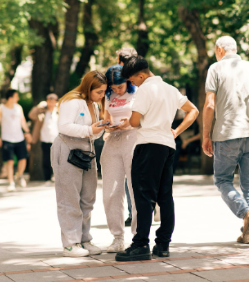 A group of teenagers using a smartphone outdoors to book a FREE NOW group ride enjoying summer leisure in a park setting.