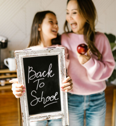Mother and daughter joyfully celebrating Back to School indoors with a blackboard and a red apple.