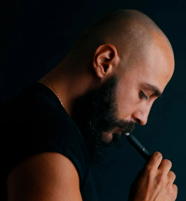 A masculine man in a black shirt using an e-cigarette