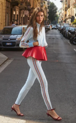 A lady walking in the street wearing a white outfit from Fiorucci with a red leather peplum