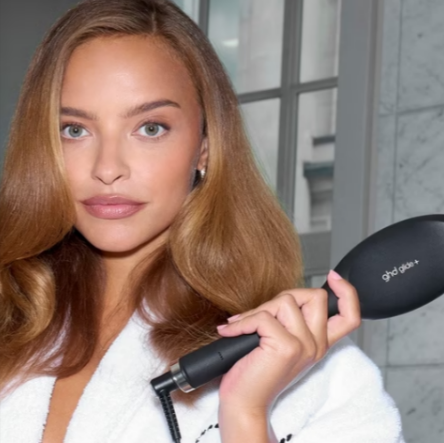 A woman using a ghd brush to style her hair in a ghd robe.