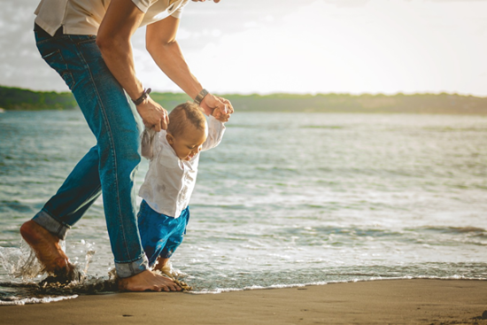 Ein Vater, der seinem Kind an einem Strand beim gehen hilft