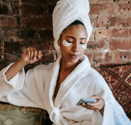 Woman in a bathrobe relaxing while reading skincare tips on the Foreo app while applying skincare patches, sitting indoors