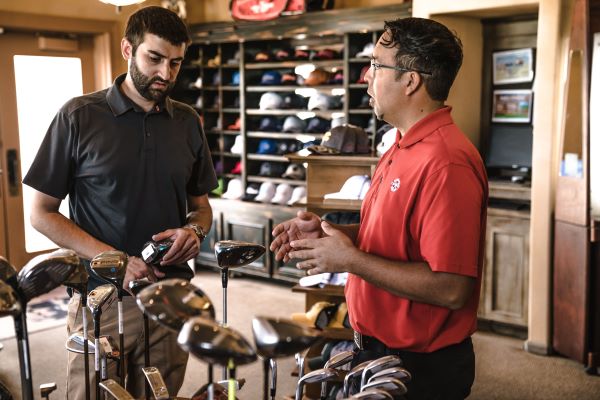 Two men standing in a golf shop with golf clubs and hats on display